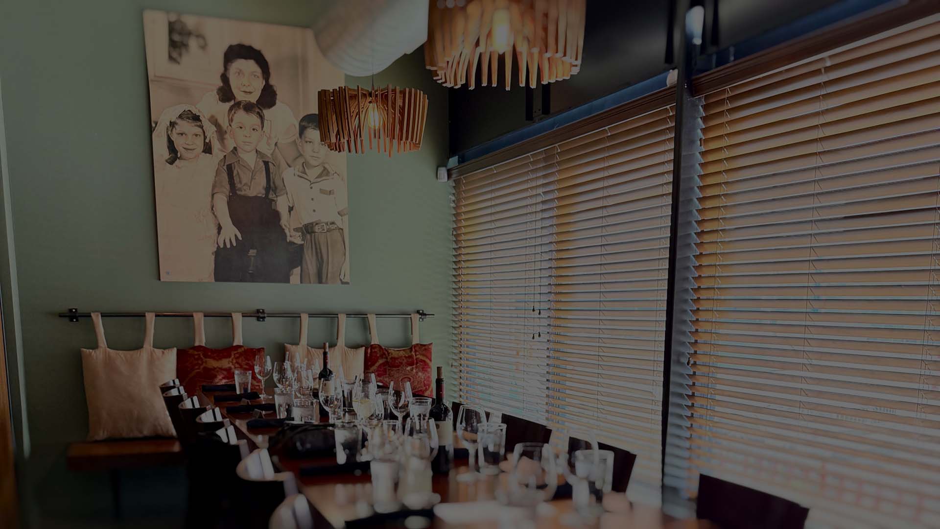 Dining room scene with a long table set with wine glasses, while a Ragazza family portrait hangs on the wall in the background